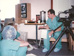 Man in scrubs next to video camera talking to people